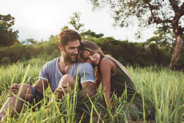 Shot of romantic young couple sitting in meadow. Man and woman relaxing together in the grass field in countryside.