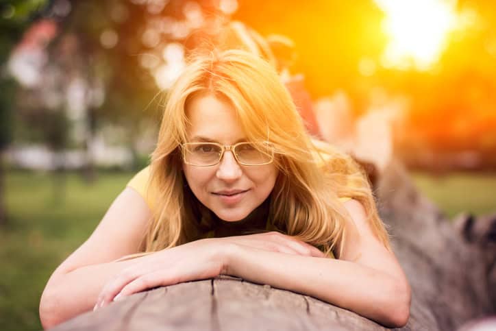Blonde girl lying on big cutted tree in forest on sunny day