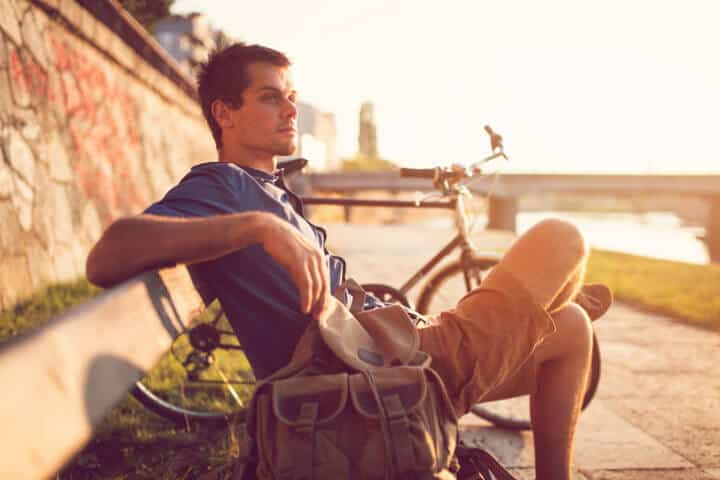 Young caucasian man sitting on the bench, enjoying a carefree summer day by the river.