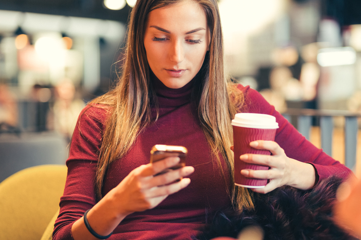 Young woman drinking coffee and texting.