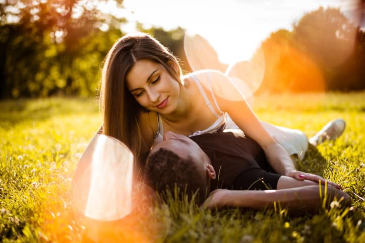 Young mixed race couple hugging in nature on grass - woman lies on man