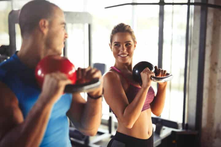 Two young atletic people are doing kettlebell exercises at the gym.