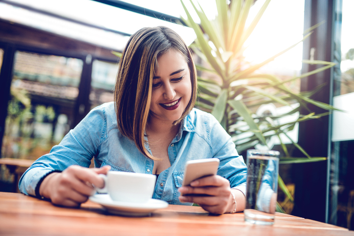 Young beautiful female using smartphone and drinking coffee at her favorite cafe place. Taking a break to connect.