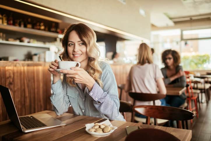 Photo of a young woman enjoying coffee with her laptop
