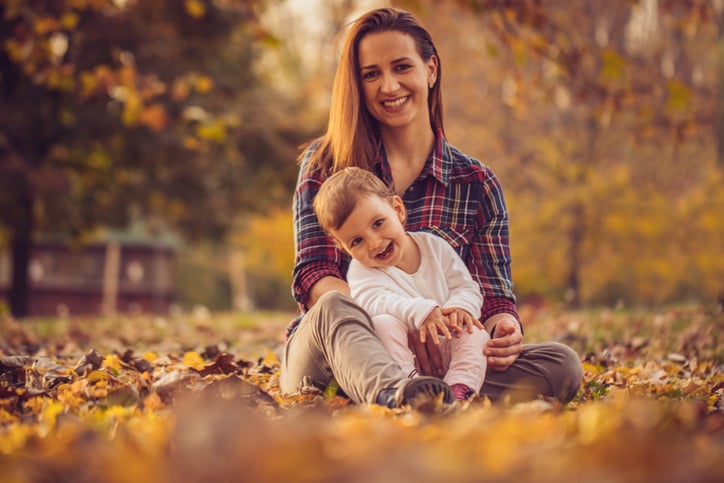 Mother and her daughter in park on a beautiful autumn day sitting on a lefs covered ground in park.