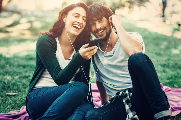 Young happy couple sitting on a blanket and listening to music outdoors.