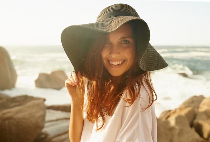 Portrait of a happy young woman wearing a hat while relaxing by the sea