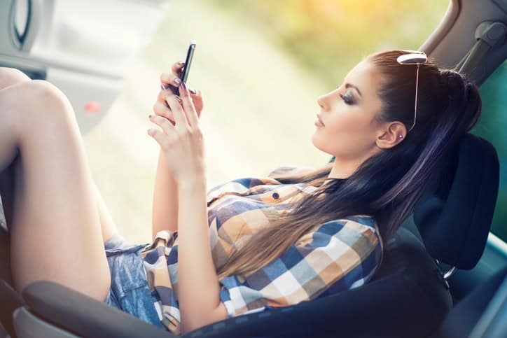 Young Sensual Woman how Using Smart phone and sitting in Car, she is wearing shirt, short pants and sunglasses.