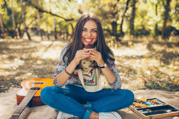Smiling teen girl sitting outdoors with guitar.