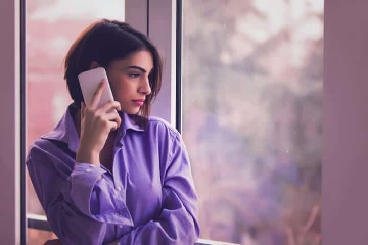Beautiful girl in mans shirt talking on the phone by the windows