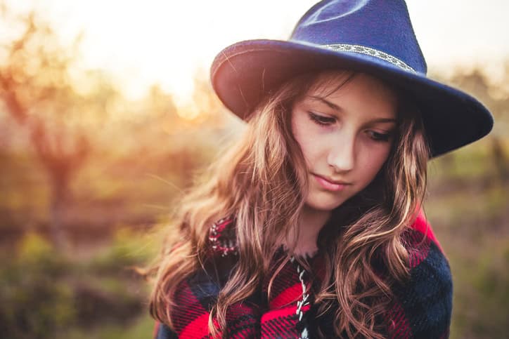 Girl with big hat enjoying in sunset wrapped in red plaid blanket