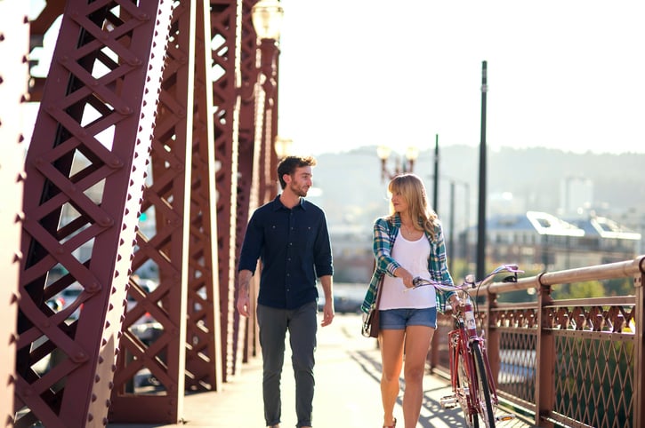Young adult heterosexual couple walking a bike along a bridge