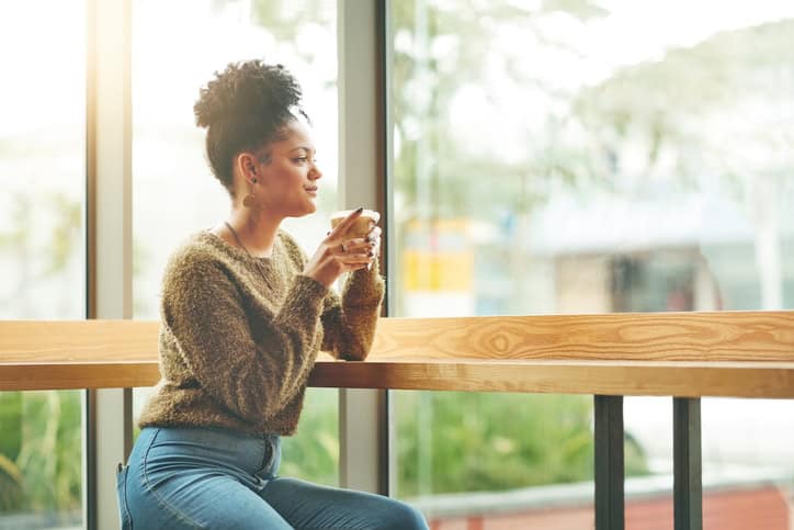 Woman sitting in cafe drinking coffee, staring out window.