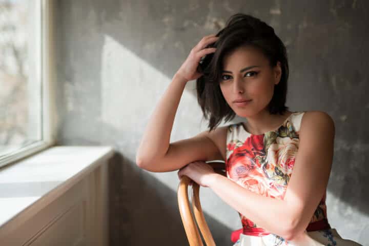 Fashion portrait of a beautiful black-haired woman sitting on a chair by the window.