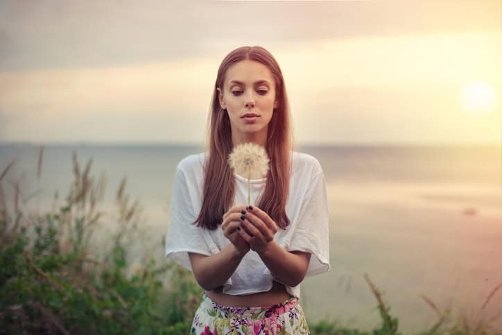 portrait of a brunette young woman with a big dandelion on a background of warm sunset. summer, outdoors.