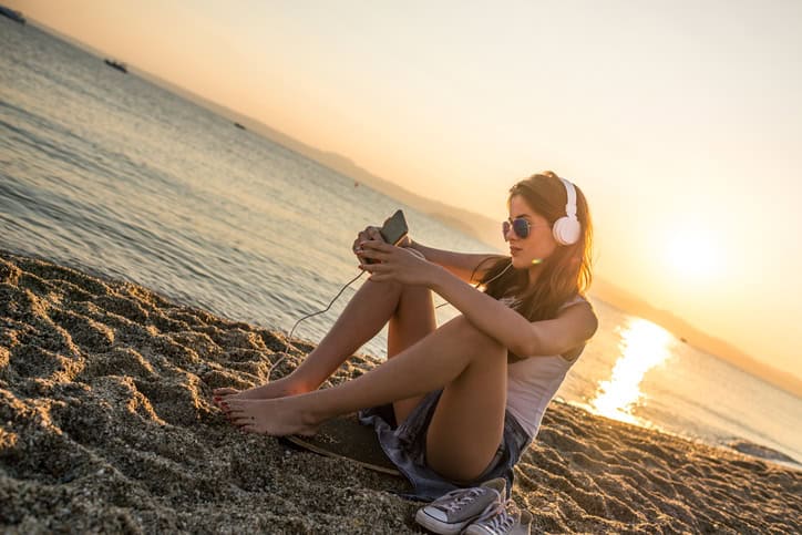 Beautiful woman listening music on smart phone at the beach