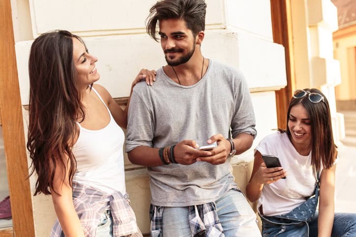 Young friends standing at the street corner and using smart phone.