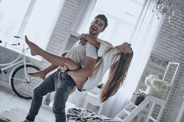 Young beautiful couple having fun at home together while man carrying his girlfriend on shoulders