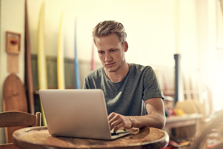 Shot of a happy young man using his laptop while relaxing at home
