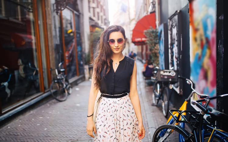 Vintage toned portrait of a young fashionable brunette, wearing sunglasses, walking in the city center of Amsterdam, Holland. She is enjoying the bright and sunny summertime day in Holland Capital, walking in the narrow streets filled with bicycles.