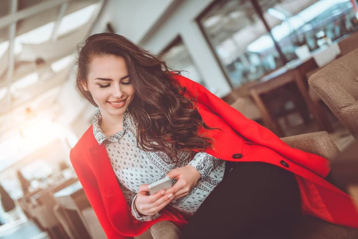 Young Brunette Woman texting on mobile smart phone, sitting in cafe restaurant and smiling.
