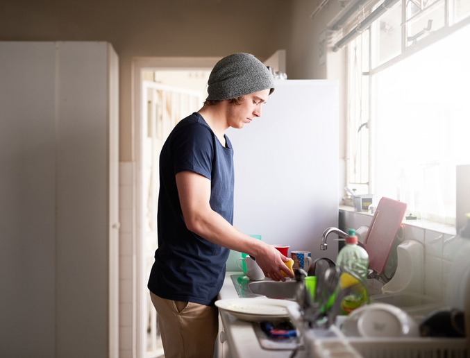 Man washing dishes in his apartment.