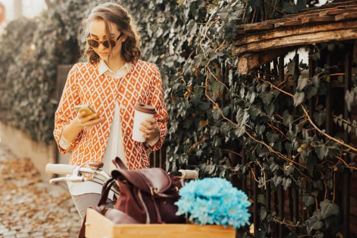 Beautifully dressed girl sitting on the bicycle using smartphone
