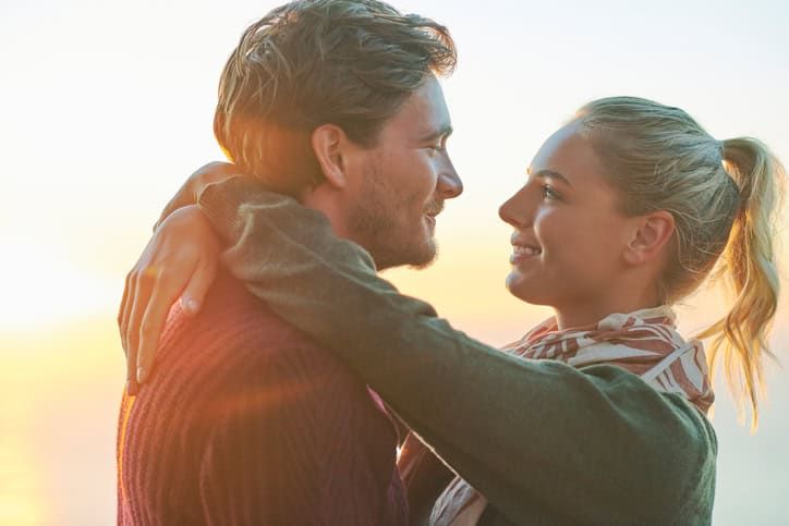 Side view of romantic young couple embracing against sky. Loving male and female partners are spending quality time together. They are wearing casuals during sunset.