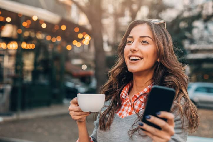Young woman using a smart phone and drinking coffee outdoors.