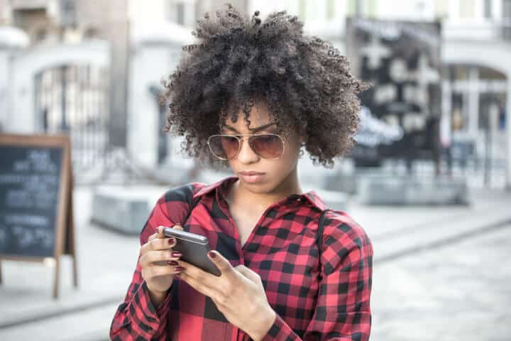 Beautiful cheerful african woman using smart phone outdoors.