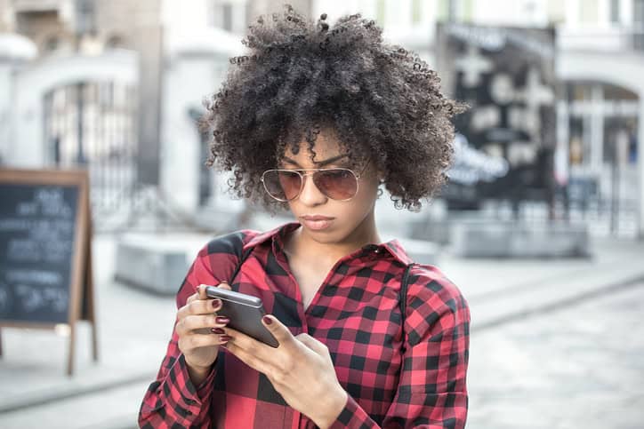 Beautiful cheerful african woman using smart phone outdoors.