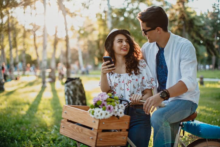 Couple with bicycle in the park, using mobile phone