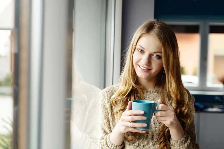Beautiful smiling blond woman drinking coffee by the window