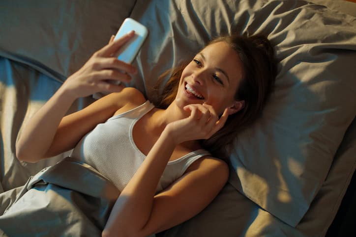 Close up of a young woman using smart phone while lying in bed