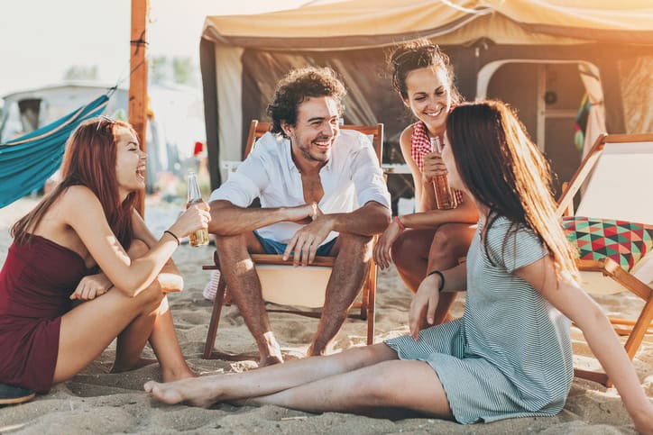 Group of young people chatting and drinking beer outdoors on a summer camp.
