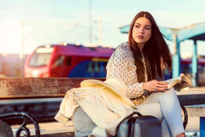 Girl on train station with luggage reading a book