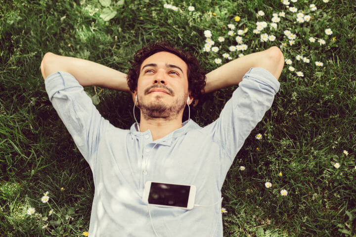 Young man relaxing in the grass and enjoying the music or podcast.
