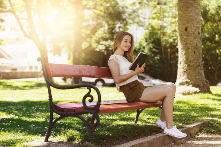 Young woman reading book on bench