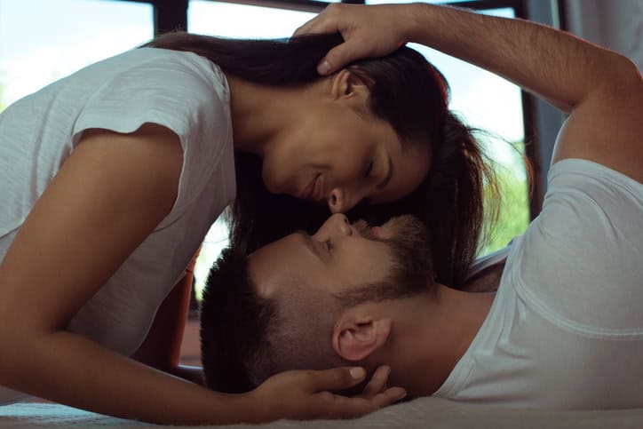 tender young couple with closed eyes hugging and kissing in bed