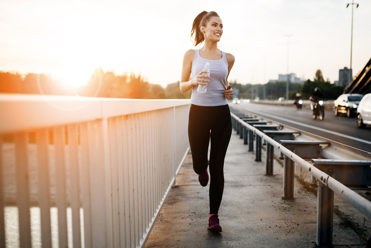 Beautiful woman running over bridge during sunset