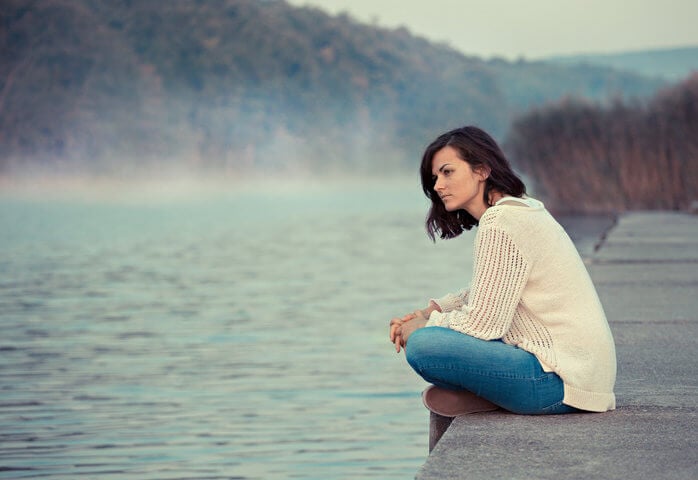 Young woman sitting by lake in the early morning.