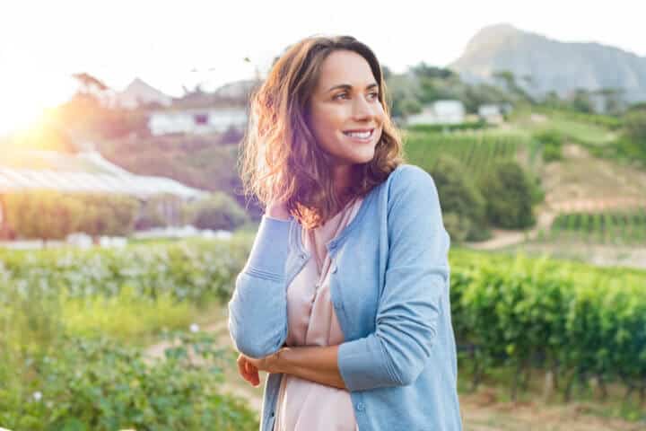 Portrait of mature brunette woman relaxing at park and looking away. Happy woman relaxing outdoor at sunset. Smiling mature woman thinking.