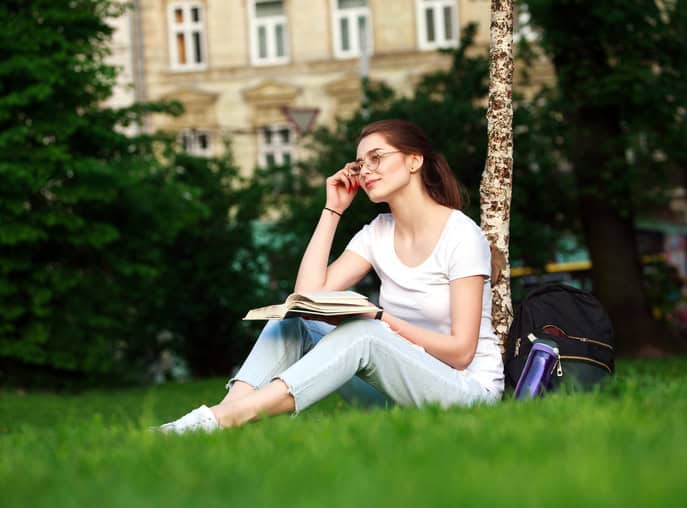 Smiling girl student in city park with book