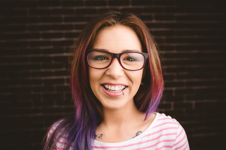 Portrait of smiling woman in spectacles against brick wall