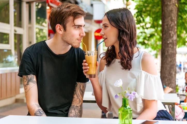 Happy couple sitting on a bench and drinking from one cup.