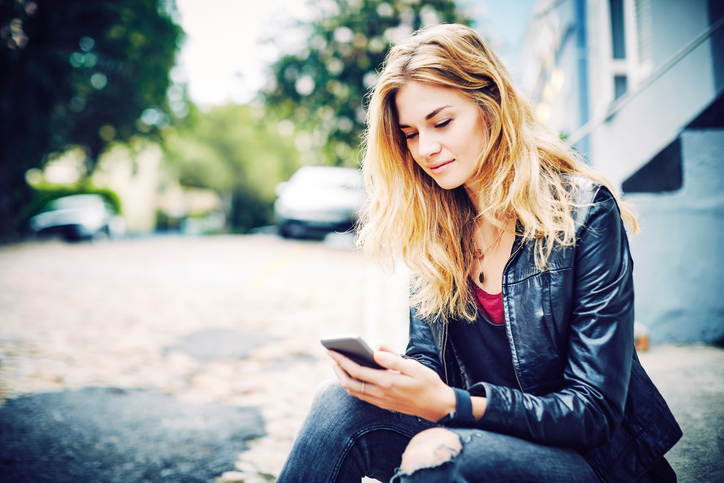Beautiful blond woman using smart phone on roadside