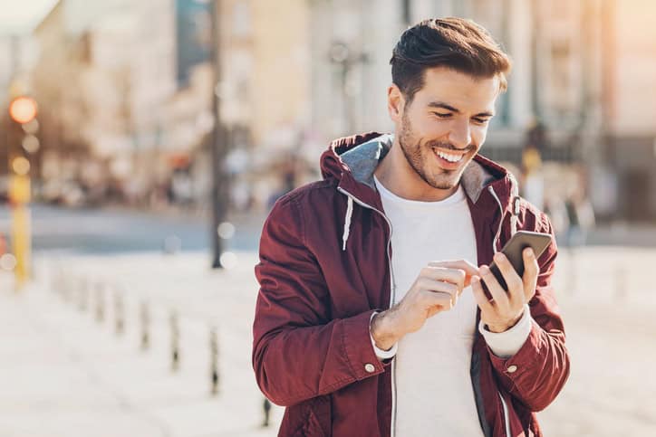 Young man with smart phone texting outdoors in the city