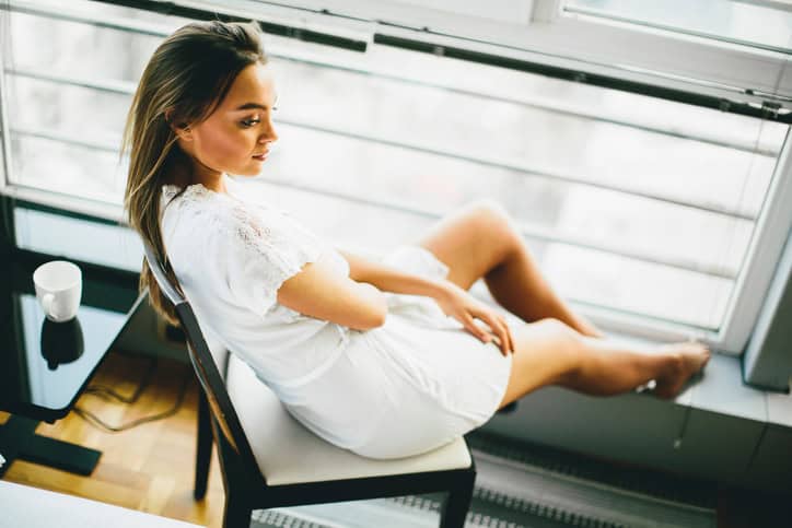 Young woman sitting and dreaming on a chair by the window in her nightgown