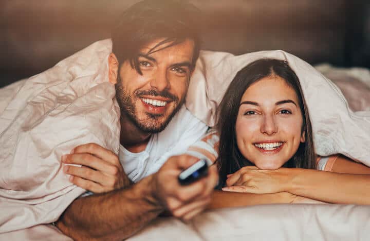 Couple watching TV in bed.