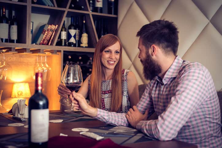 Two young people waiting for dinner and drinking wine. Couple in restaurant celebrating their love with smiles on their faces
